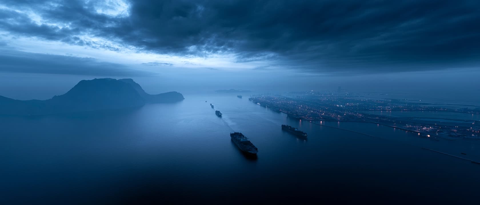 Aerial view of cargo vessels navigating a deep-water harbour at pre-dawn — expressing the scale of Golden Falcon International's global trade and strategic maritime operations